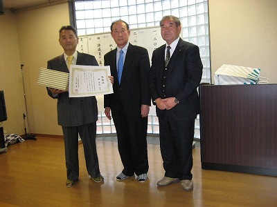 「退任される鄭英道氏（左）に金有作理事長（中央）から感謝状並びに記念品が贈呈された」